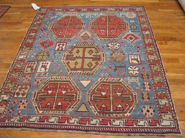 Geometric red and tan hexagonal medallions decorate a blue tribal rug on hardwood flooring.