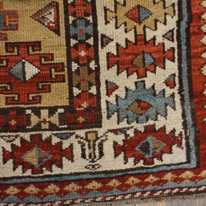 Muted geometric rug corner with red, slate blue, and khaki motifs sits on distressed wood flooring.
