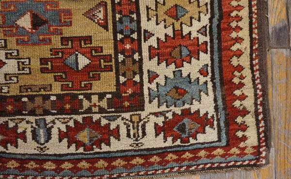 Muted geometric rug corner with red, slate blue, and khaki motifs sits on distressed wood flooring.