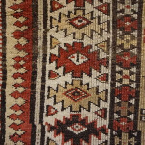 Geometric rug detail showing textured stripes in red, tan, cream, and brown next to wood planks.
