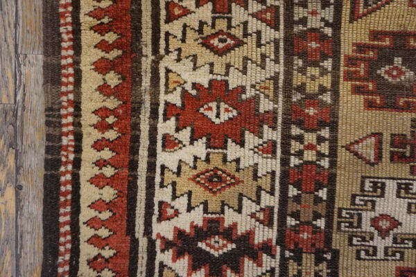 Geometric rug detail showing textured stripes in red, tan, cream, and brown next to wood planks.