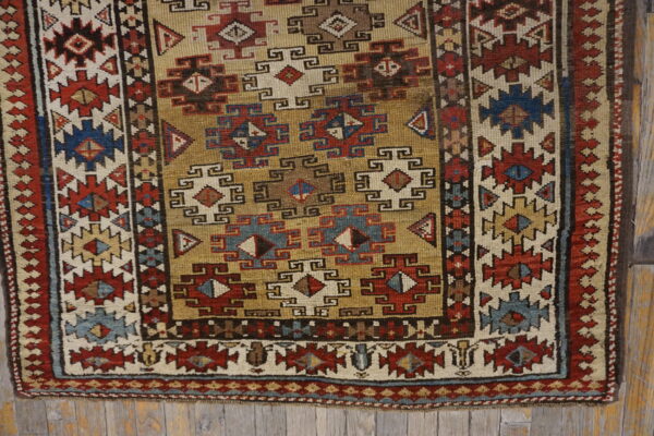 Low-pile rug with geometric patterns in gold, brick red, navy blue, and cream on weathered wooden planks.