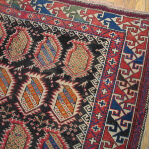 Rustic geometric rug patterned in black, red, blue, and orange resting on light wooden floorboards.