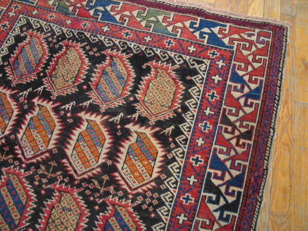 Rustic geometric rug patterned in black, red, blue, and orange resting on light wooden floorboards.