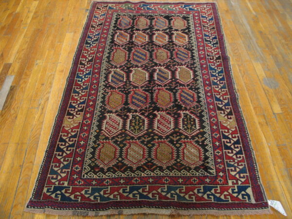 A dark, rectangular, geometric rug with red and blue borders and repeated medallion motifs on wood flooring.