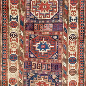 Narrow rug with alternating geometric star and meander motifs in red, indigo, brown, and cream.