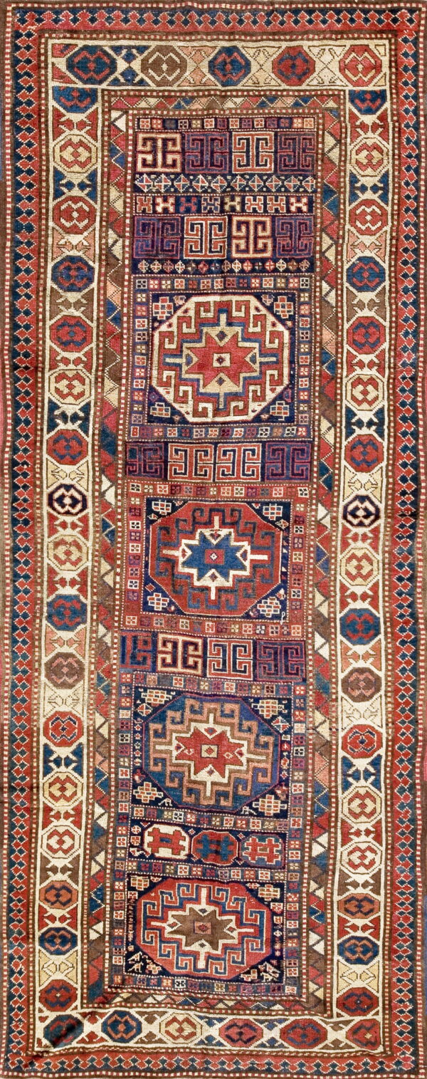 Narrow rug with alternating geometric star and meander motifs in red, indigo, brown, and cream.