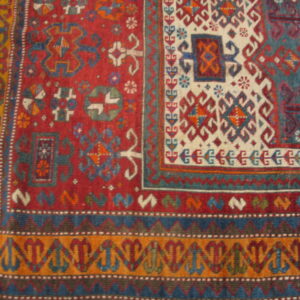Multi-colored geometric rug detail in red, cream, blue, and orange sits upon light brown wooden floor.