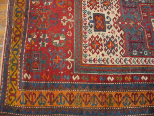 Multi-colored geometric rug detail in red, cream, blue, and orange sits upon light brown wooden floor.