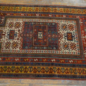 Red, blue, and gold patterned rug with a diamond medallion sits on distressed wooden flooring.