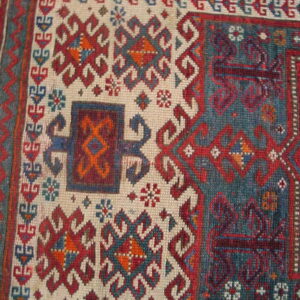 Tribal geometric rug detail in red, teal, blue, and cream with stylized latch-hook patterns.