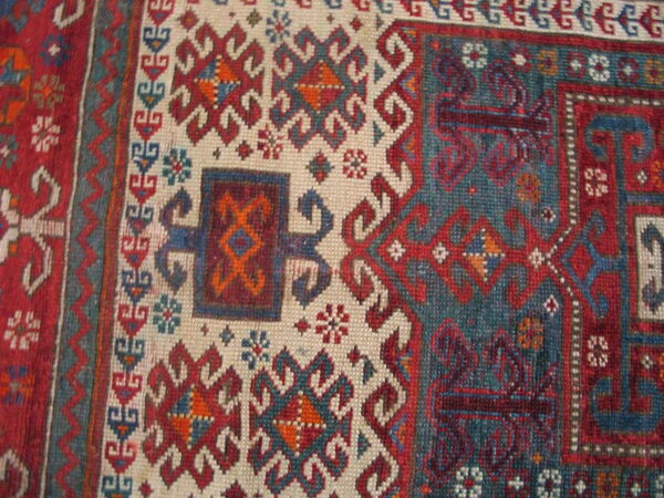 Tribal geometric rug detail in red, teal, blue, and cream with stylized latch-hook patterns.