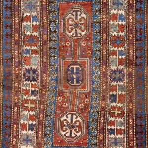 Intricately patterned low-pile rug dominated by deep red, cobalt blue, brown, and cream geometric tribal motifs.