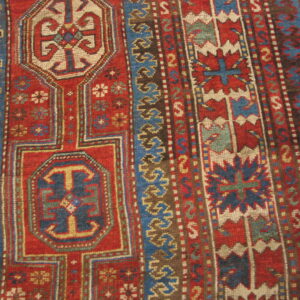 Close-up of a rug featuring red, blue, and cream geometric tribal motifs on a wood floor.