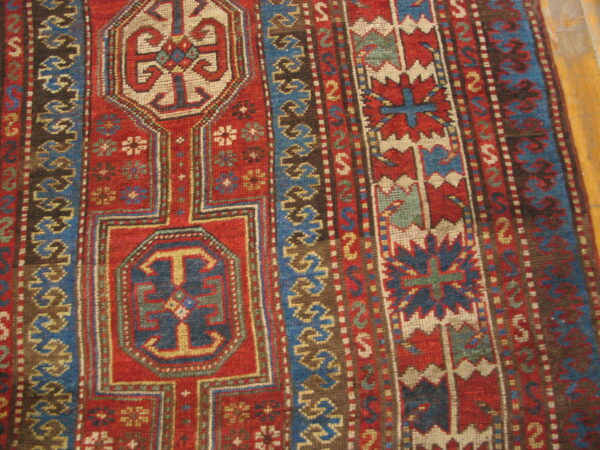 Close-up of a rug featuring red, blue, and cream geometric tribal motifs on a wood floor.