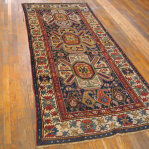 Low-pile runner rug with a navy, red, and multicolor geometric pattern on distressed wood planks.