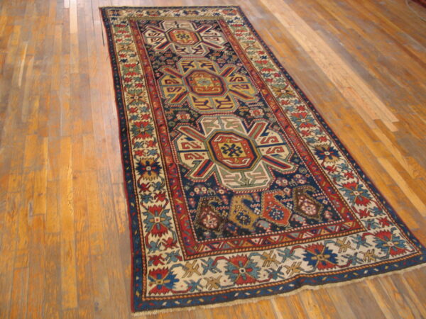Low-pile runner rug with a navy, red, and multicolor geometric pattern on distressed wood planks.