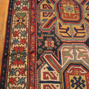 Geometric patterned rug in deep navy, red, mustard, and cream, lying on light plank flooring.