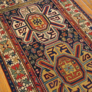 Low pile rug with geometric medallions in navy, red, and gold colors on hardwood flooring.