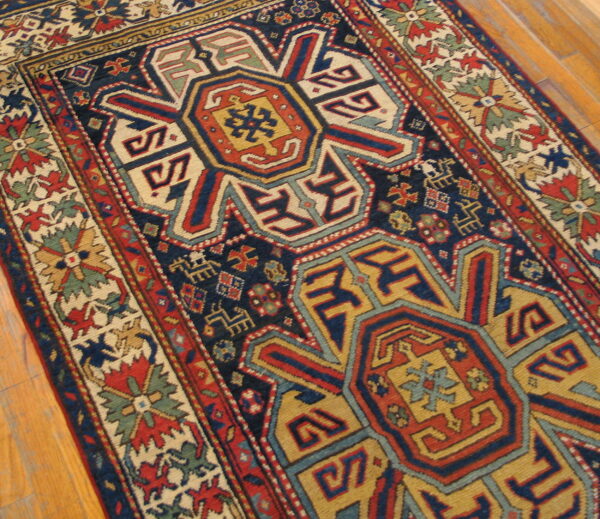 Low pile rug with geometric medallions in navy, red, and gold colors on hardwood flooring.