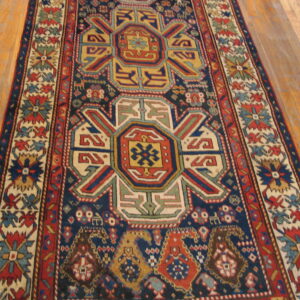 A dark blue geometric runner with medallions in red, yellow, and cream lies on light hardwood flooring.