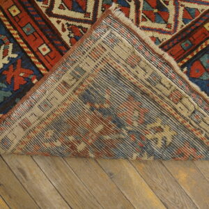 Geometric red and blue patterned rug with low pile turned back to show woven backing on wood planks.