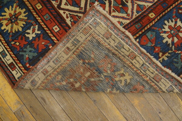 Geometric red and blue patterned rug with low pile turned back to show woven backing on wood planks.