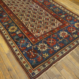 Low-pile rug with a cream lattice field and a blue border, laid on rustic hardwood flooring.