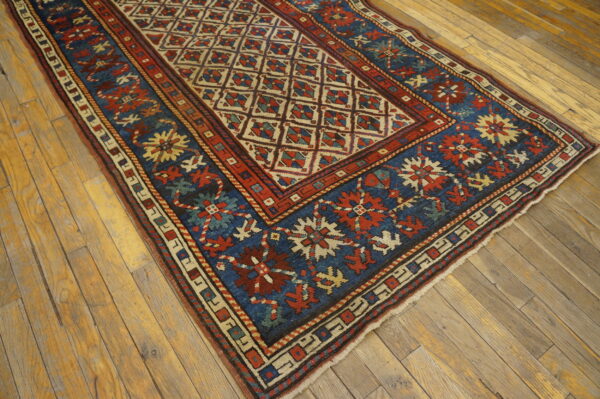 Low-pile rug with a cream lattice field and a blue border, laid on rustic hardwood flooring.