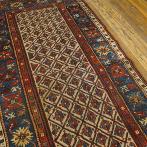 Low pile runner in red and blue geometric patterns rests on yellow-toned plank wood flooring.