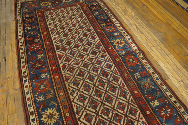 Low pile runner in red and blue geometric patterns rests on yellow-toned plank wood flooring.