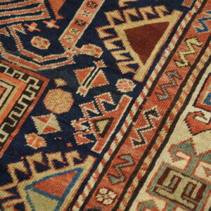 Navy blue and coral geometric rug showing detailed motifs and a multicolored complex border on wood flooring.