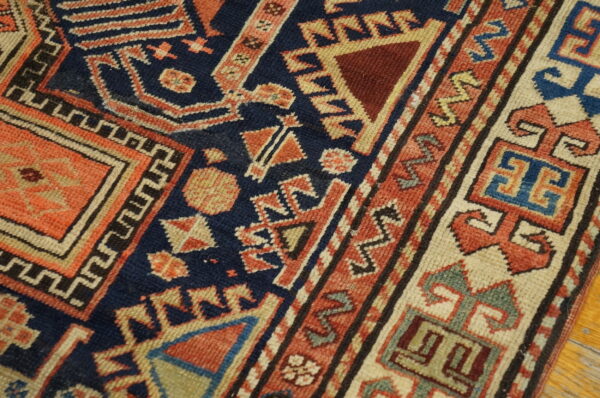 Navy blue and coral geometric rug showing detailed motifs and a multicolored complex border on wood flooring.