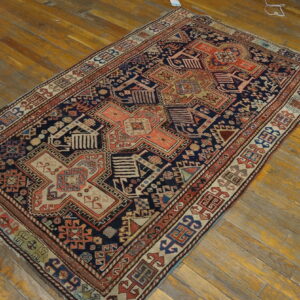 A navy and coral geometric pattern rug with beige accents is displayed on worn, yellowish-orange wood planks.