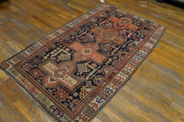 A navy and coral geometric pattern rug with beige accents is displayed on worn, yellowish-orange wood planks.
