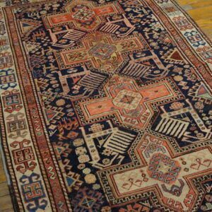 Deep blue and rust geometric rug with intricate patterns displayed on a natural wood floor.