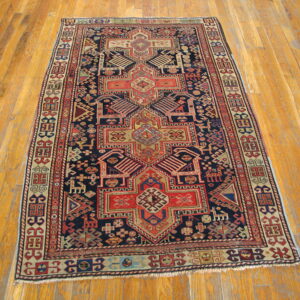 Navy, red, and beige geometric tribal rug featuring a central motif, displayed on wood plank flooring.