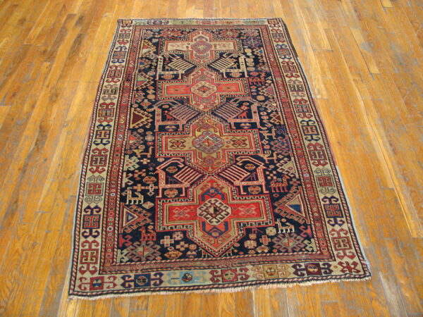 Navy, red, and beige geometric tribal rug featuring a central motif, displayed on wood plank flooring.