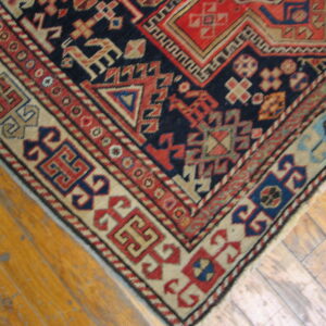 Navy, red, and beige geometric tribal rug corner with complex borders on light brown plank floorboards.