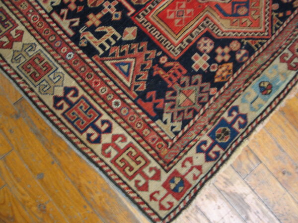 Navy, red, and beige geometric tribal rug corner with complex borders on light brown plank floorboards.