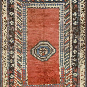 Red rug with an octagonal center motif and dense borders featuring geometric designs in blue, cream, and brown.