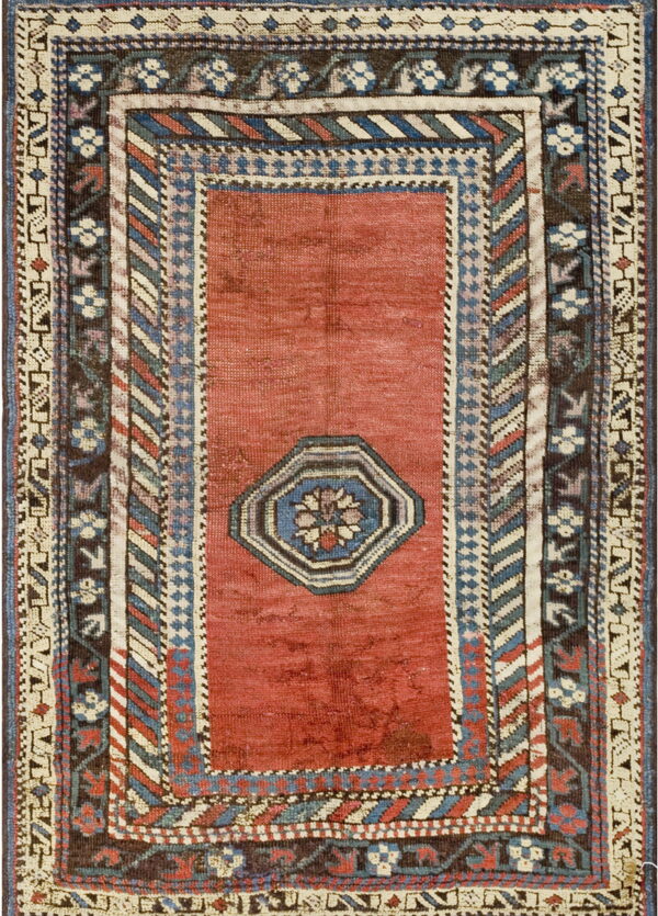 Red rug with an octagonal center motif and dense borders featuring geometric designs in blue, cream, and brown.