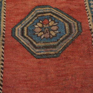 A close view of a rust-red rug field with a central octagonal blue and beige floral medallion.