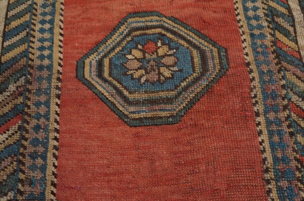 A close view of a rust-red rug field with a central octagonal blue and beige floral medallion.