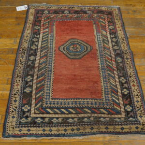 Rustic red central medallion rug with multicolored geometric borders sits on distressed wooden planks.