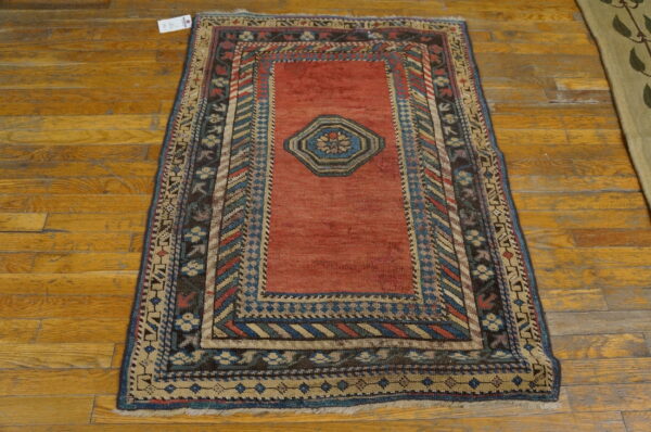 Rustic red central medallion rug with multicolored geometric borders sits on distressed wooden planks.