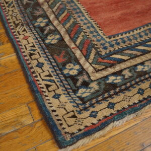 Geometric blue, tan, and dark border surrounding a coral field, lying on distressed hardwood.