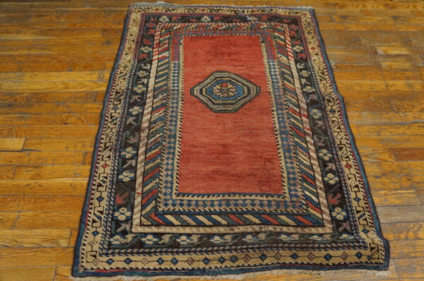 Red field rug featuring a blue medallion and multicolored geometric borders on aged wooden flooring.