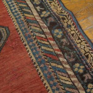 Red rug with a multi-colored geometric border and blue medallion section on worn wood flooring.