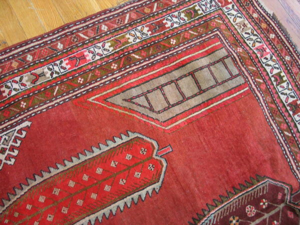 Distressed red geometric rug displaying complex borders and angular motifs on light hardwood flooring.